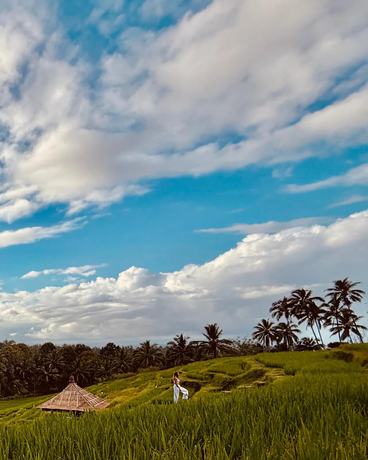 Ramona in einem weissen Kleid in den Reisterrassen auf Bali, unter weitem Wolkenhimmel.